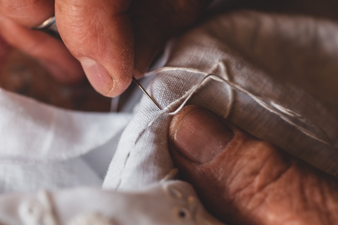 Hands stitching a visible mending patch onto wool fabric